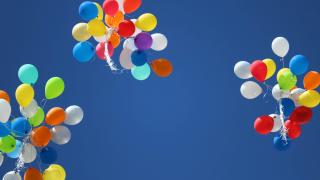 Three bunches of colorful balloons floating upward in a clear blue sky.